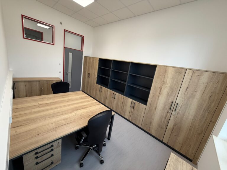 Zwei gegenüberstehende Schreibtische in Eiche-Optik mit schwarzen Bürodrehstühlen, Rollcontainer und langer Schrankwand mit offenen Regalfächern in Anthrazit